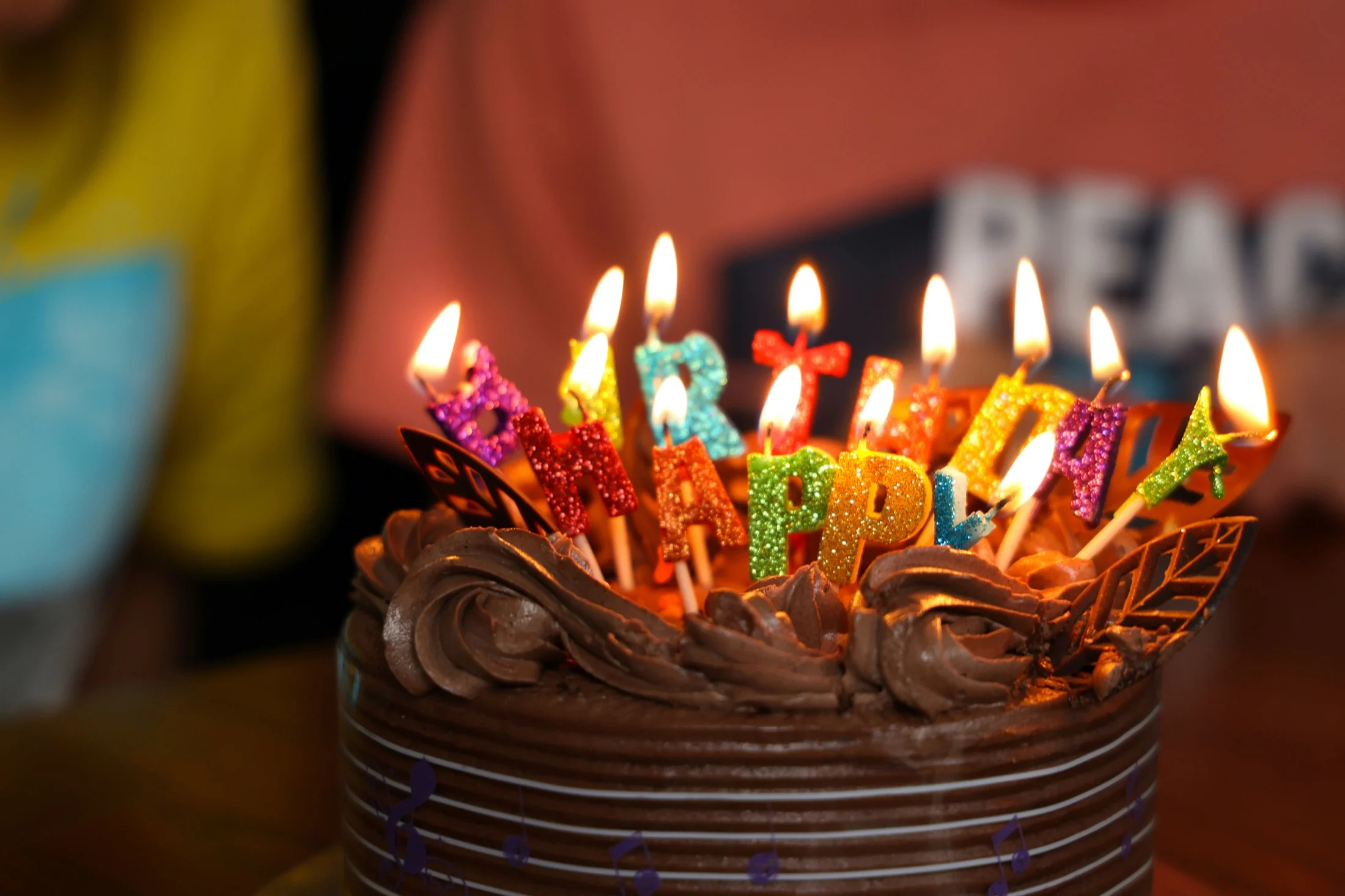 A chocolate birthday cake topped with lit, colorful HAPPY BIRTHDAY candles