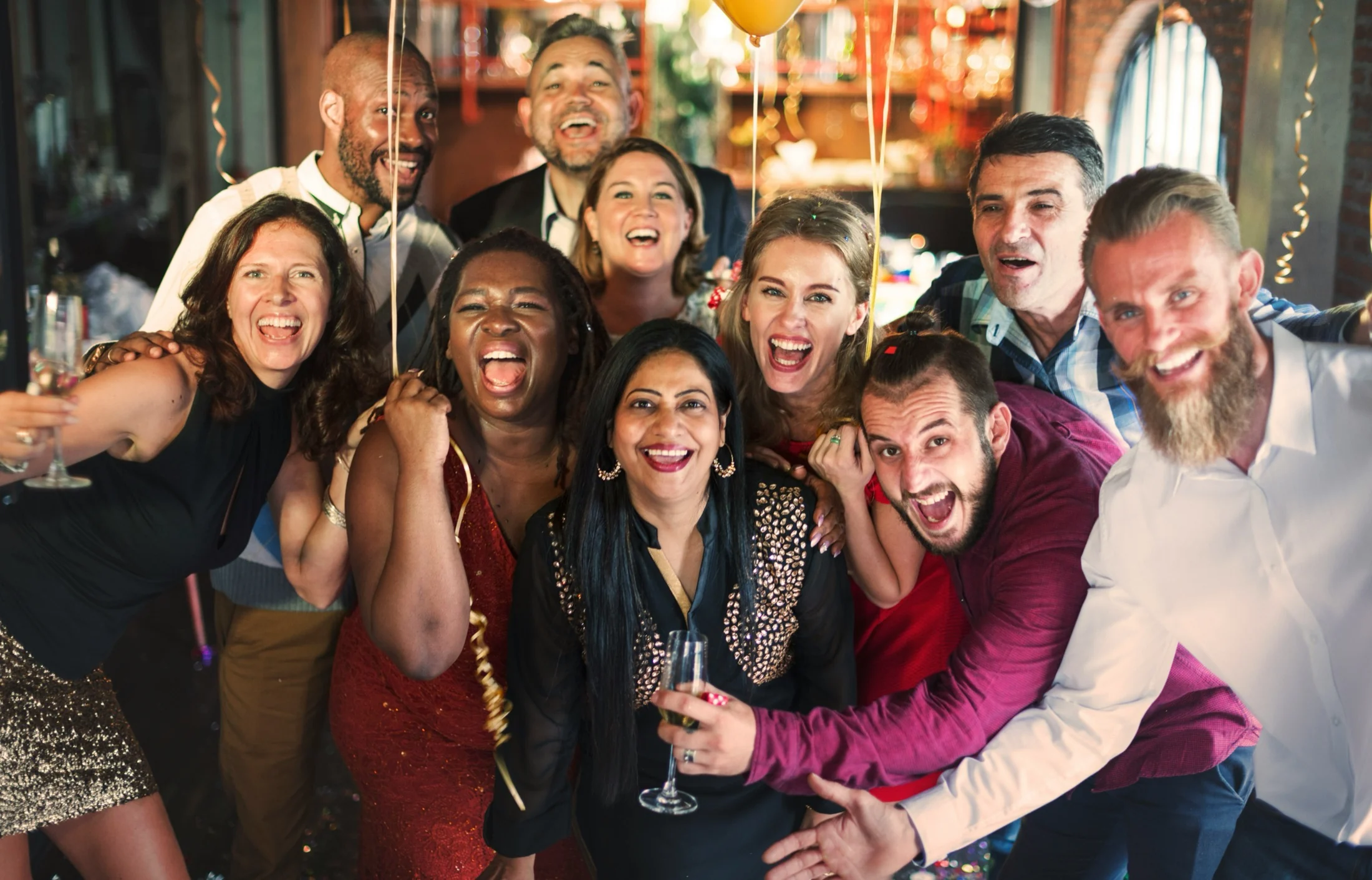 A lively group of friends and coworkers laughing and celebrating together with champagne and balloons