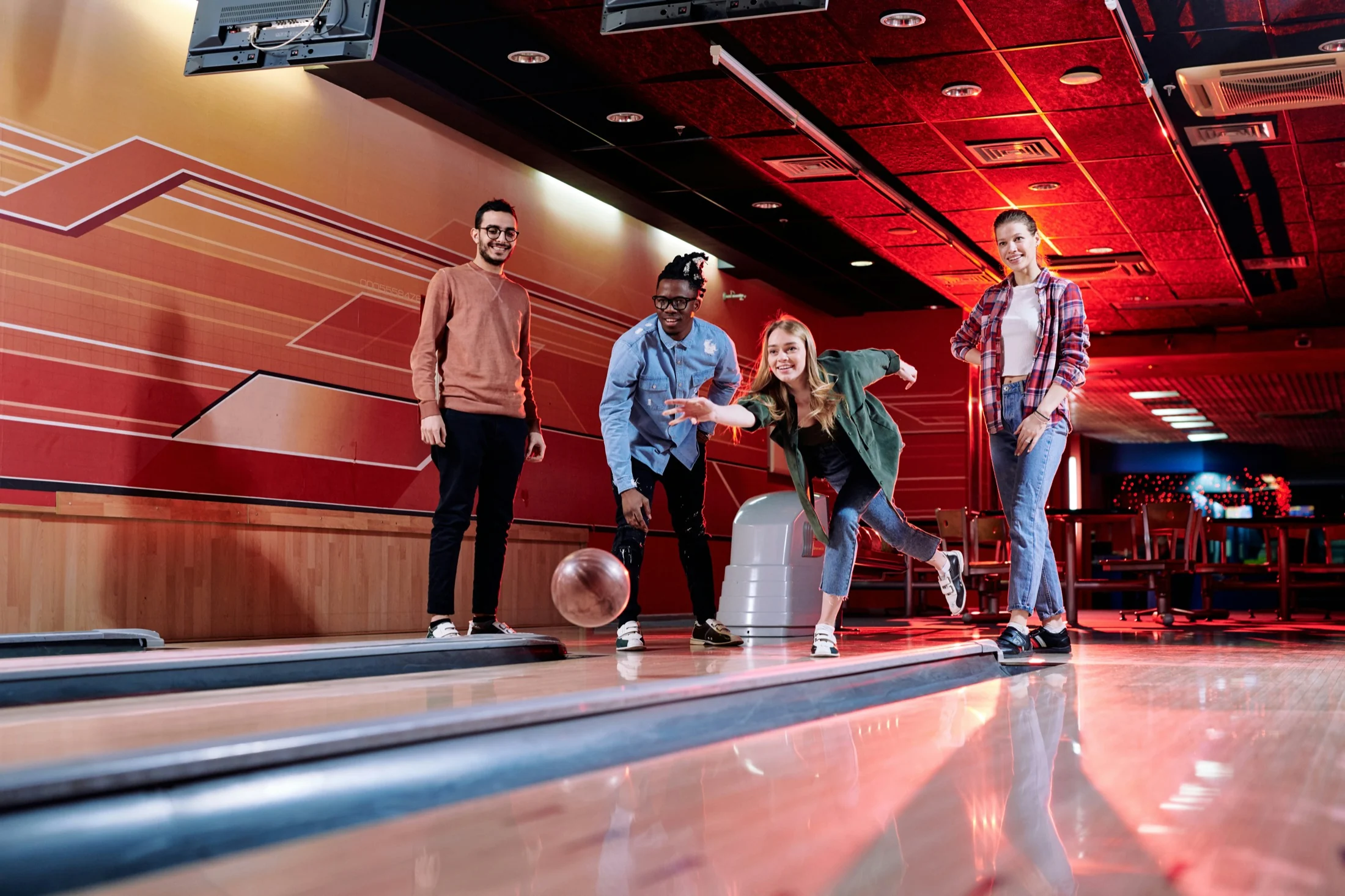 Four friends bowling together as one releases her ball down the lane, the others cheering her on