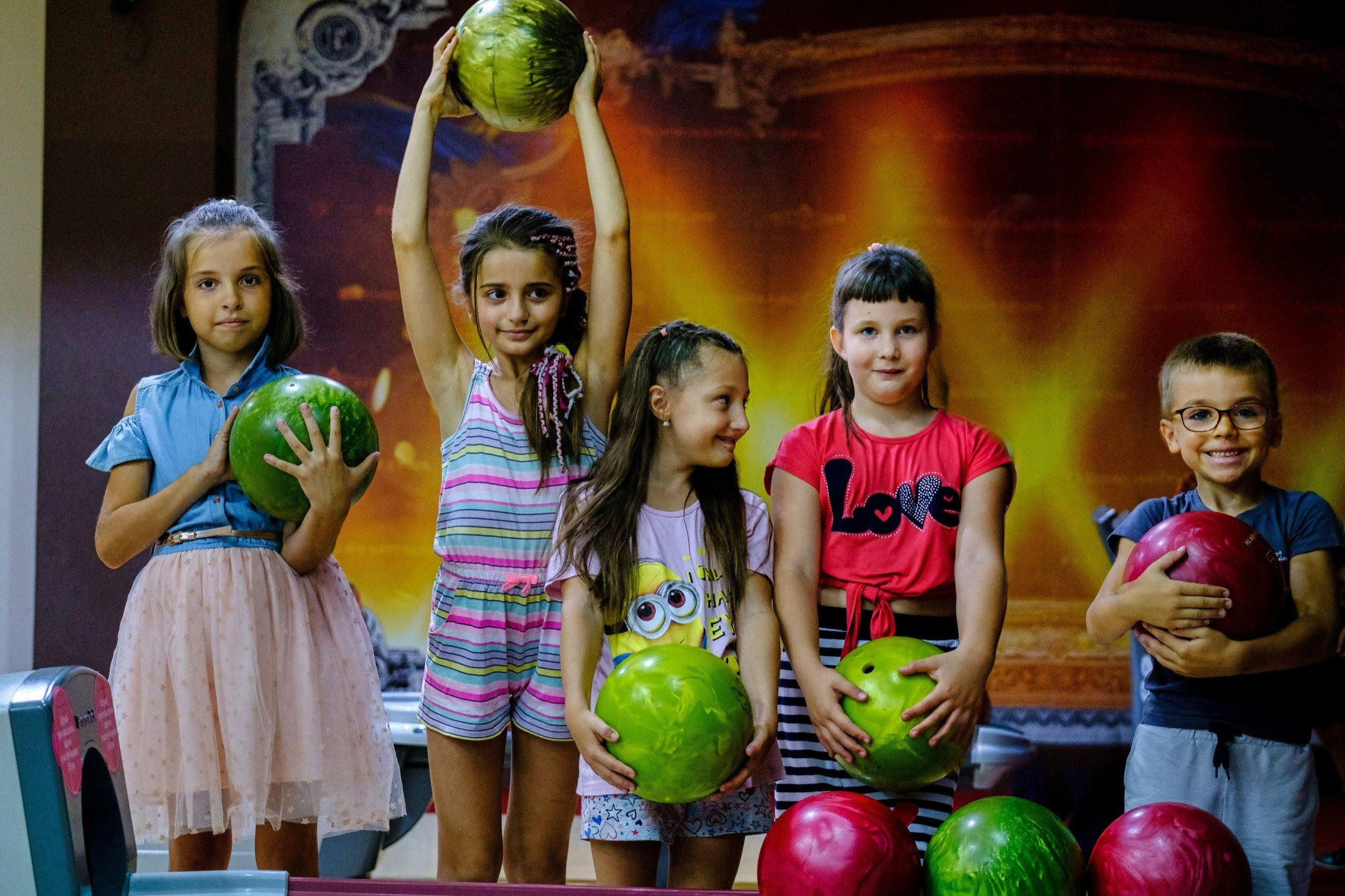 A group of smiling young Jr Pros bowlers holding colorful bowling balls at the lanes