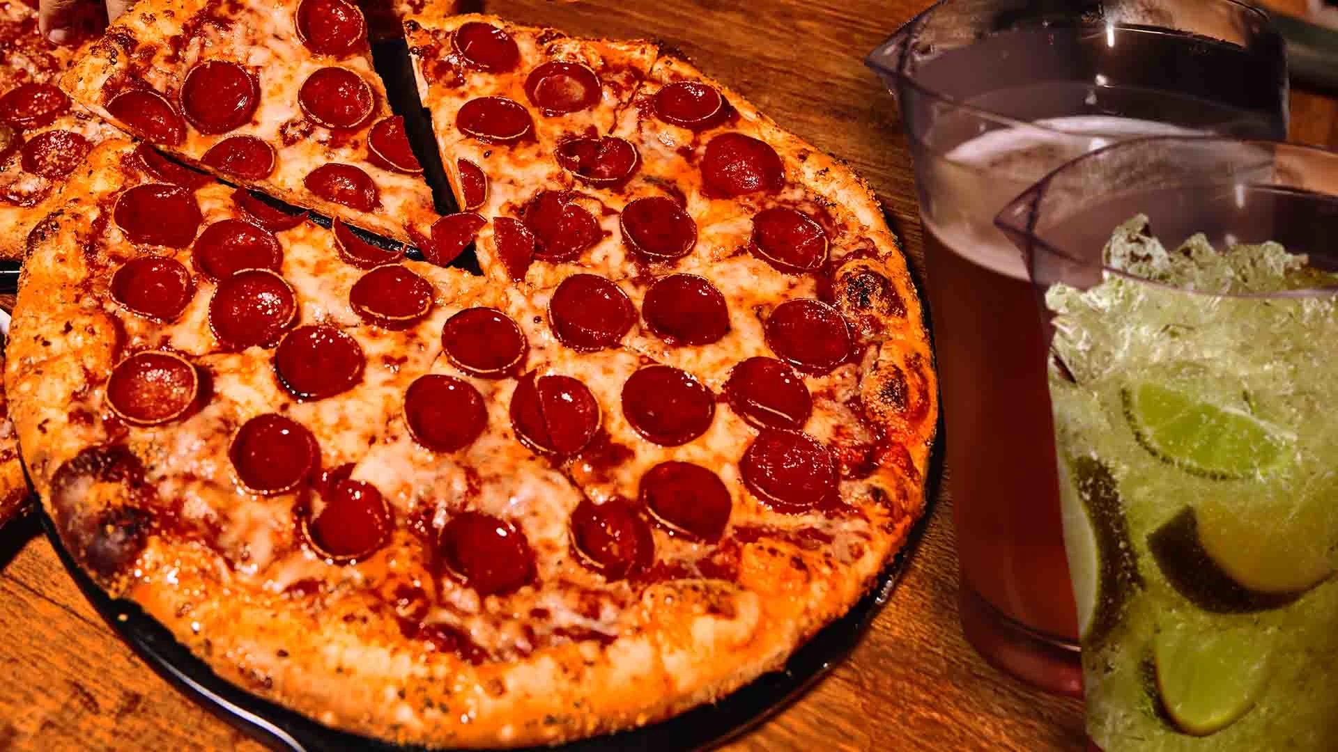 Fresh pepperoni pizza with pitchers of beer and a lime cocktail