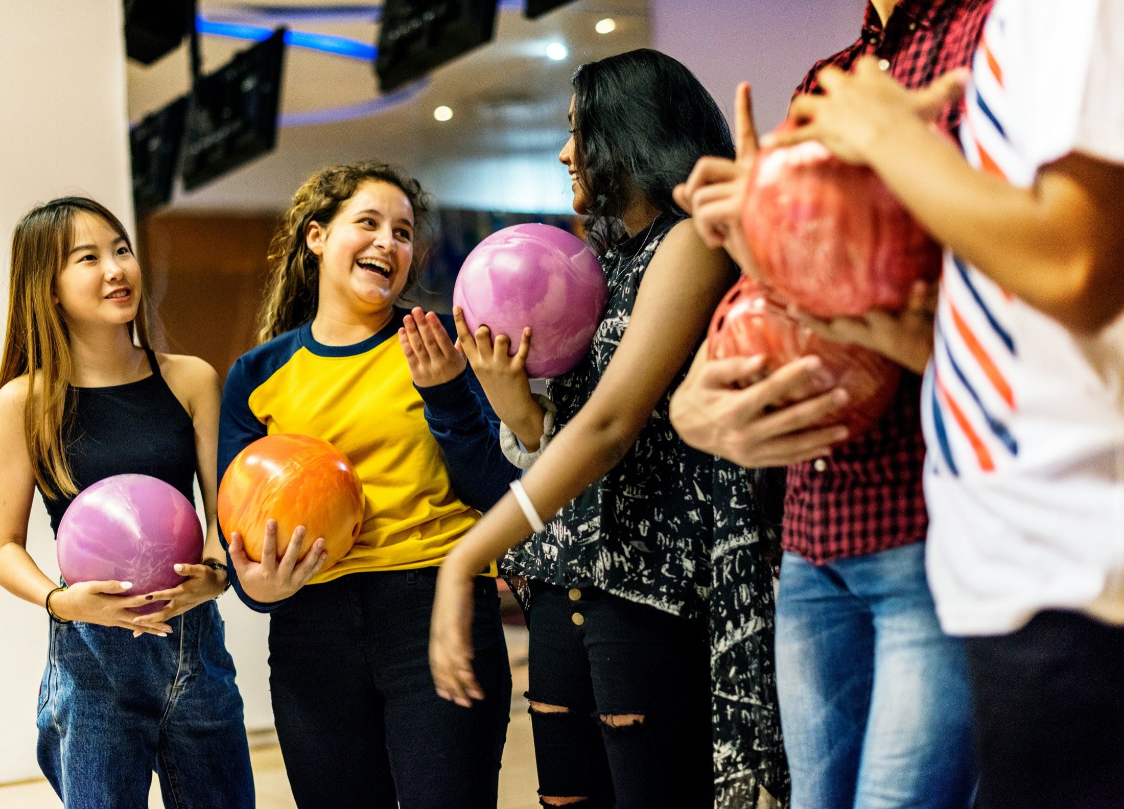 A group of young bowlers laughing together while holding their bowling balls
